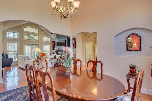 dining room with ornate columns, arched walkways, a chandelier, and wood finished floors