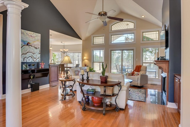 living area featuring high vaulted ceiling, decorative columns, light wood finished floors, and ceiling fan with notable chandelier