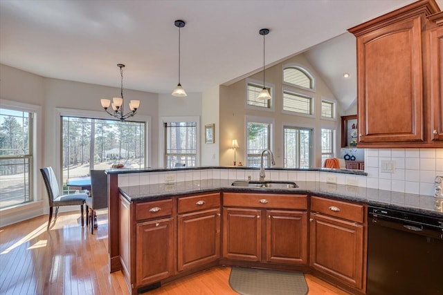 kitchen featuring light wood finished floors, tasteful backsplash, a sink, dark stone countertops, and dishwasher