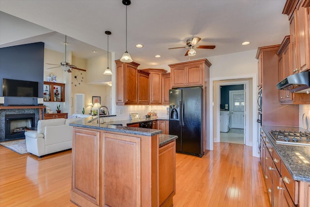 kitchen with stainless steel gas cooktop, black refrigerator with ice dispenser, a sink, a peninsula, and under cabinet range hood