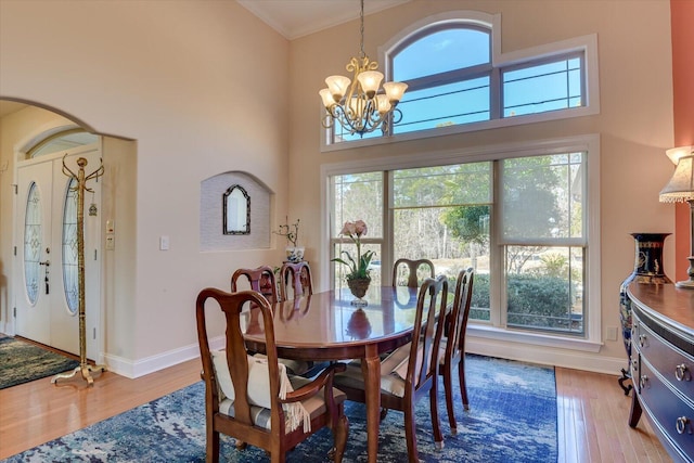 dining room with arched walkways, crown molding, a notable chandelier, a high ceiling, and wood finished floors