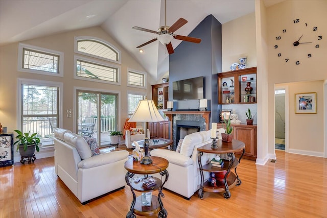 living room featuring high vaulted ceiling, a premium fireplace, a ceiling fan, baseboards, and light wood-type flooring