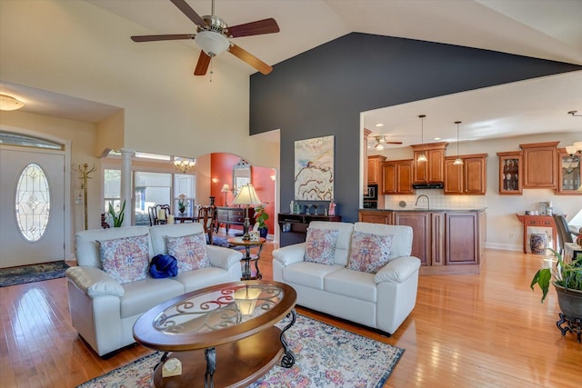 living room with high vaulted ceiling, ceiling fan, light wood-style flooring, and ornate columns