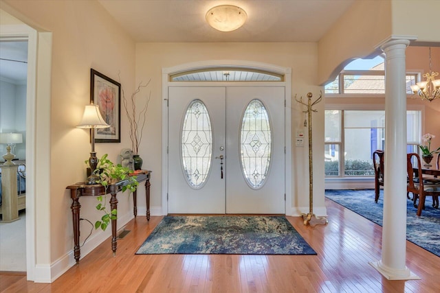 foyer entrance featuring a chandelier, baseboards, hardwood / wood-style floors, and ornate columns