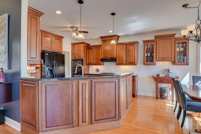 kitchen with dark stone counters, brown cabinetry, black fridge with ice dispenser, built in microwave, and light wood-style floors