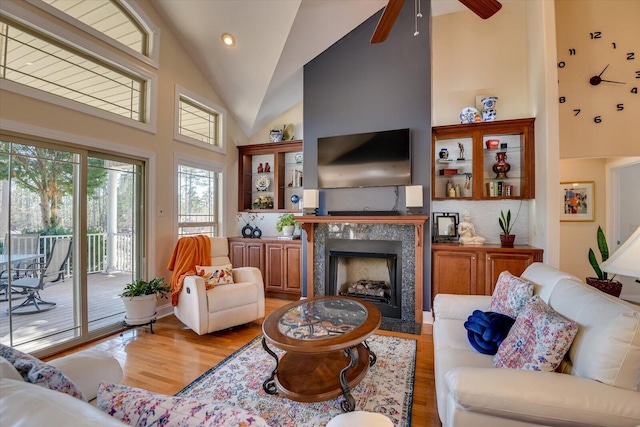 living room featuring high vaulted ceiling, a fireplace, light wood-style flooring, and a ceiling fan