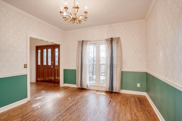 entryway with wallpapered walls, a chandelier, a wainscoted wall, and wood finished floors