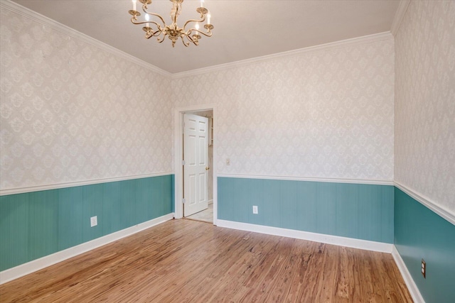 unfurnished room featuring wallpapered walls, an inviting chandelier, wood finished floors, and wainscoting