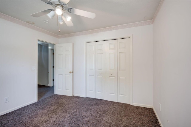 unfurnished bedroom featuring baseboards, a ceiling fan, dark colored carpet, crown molding, and a closet