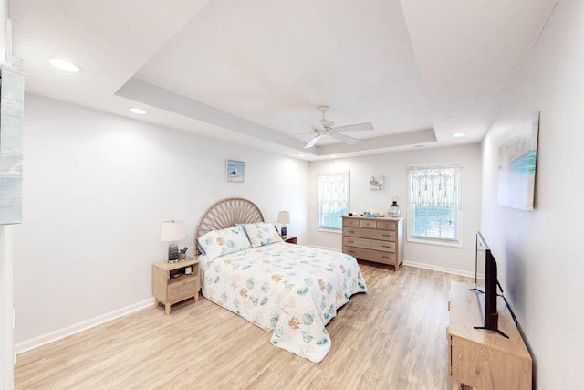 bedroom with a raised ceiling, ceiling fan, and light hardwood / wood-style floors