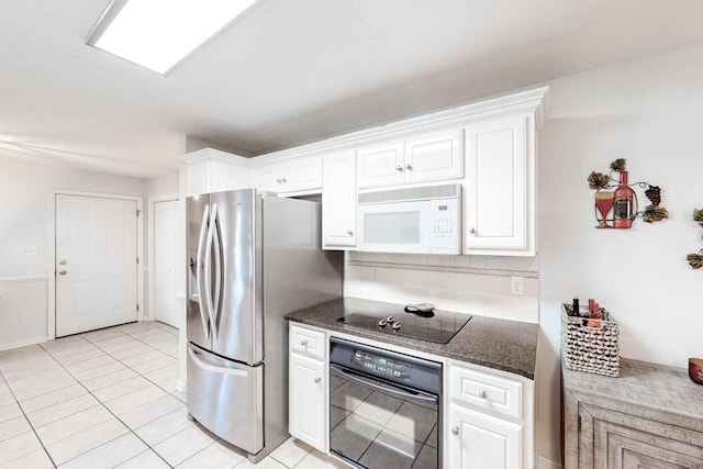 kitchen featuring dark stone counters, black appliances, light tile patterned floors, tasteful backsplash, and white cabinetry