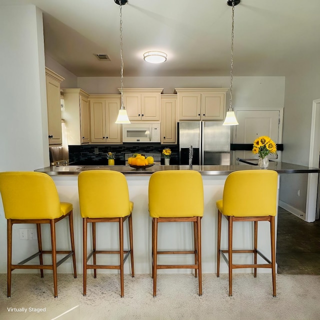 kitchen featuring stainless steel fridge, visible vents, white microwave, cream cabinetry, and backsplash