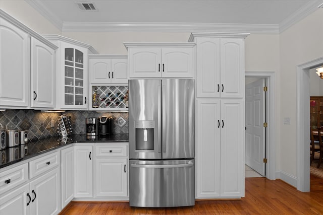 kitchen with visible vents, dark stone counters, light wood-style flooring, glass insert cabinets, and stainless steel refrigerator with ice dispenser