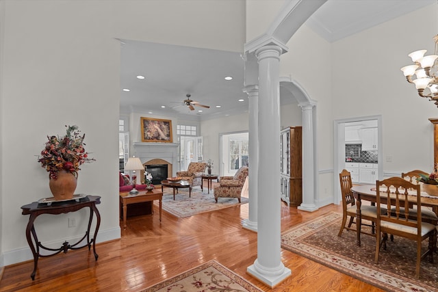 entrance foyer featuring arched walkways, a glass covered fireplace, light wood-style flooring, and ornate columns