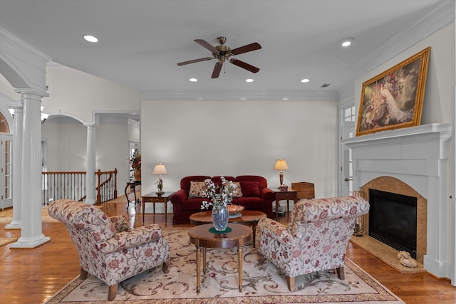 living area with ceiling fan, decorative columns, wood finished floors, and ornamental molding