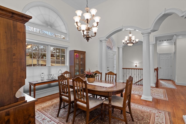 dining space with wood finished floors, a towering ceiling, arched walkways, decorative columns, and a chandelier