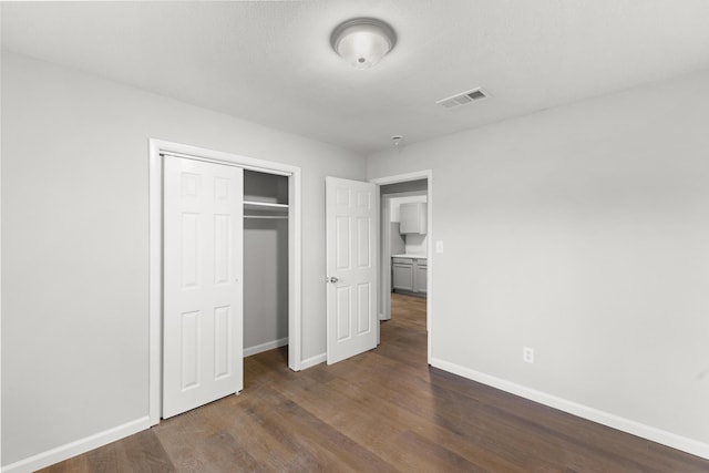 unfurnished bedroom with dark wood-style floors, a closet, visible vents, and baseboards