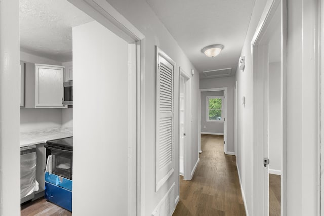 hallway featuring dark wood-style floors, attic access, visible vents, and baseboards