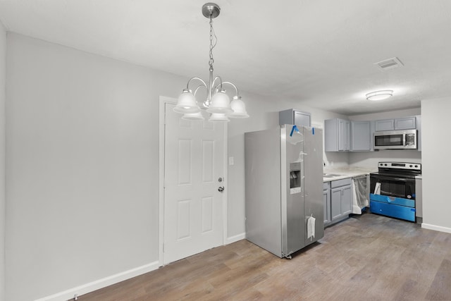 kitchen featuring gray cabinetry, light wood-style floors, light countertops, appliances with stainless steel finishes, and decorative light fixtures