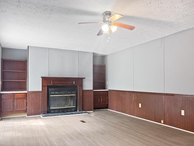 4112 Quail Farm Rd, Thomson, GA 30824 - unfurnished living room with wainscoting, a textured ceiling, a glass covered fireplace, a ceiling fan, and wood finished floors