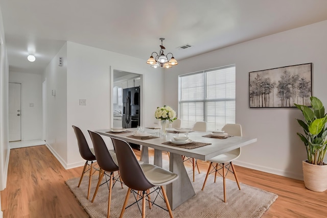 dining space with light hardwood / wood-style floors and an inviting chandelier