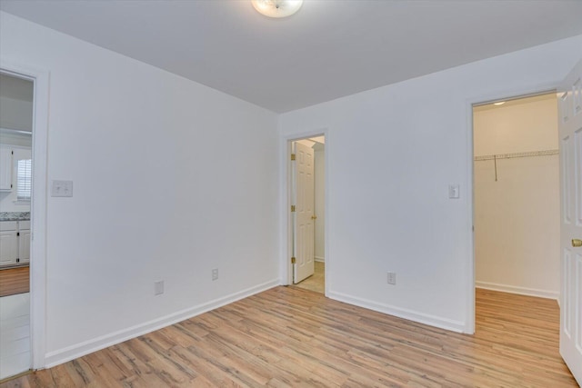 unfurnished bedroom with light wood-type flooring, a spacious closet, and a closet