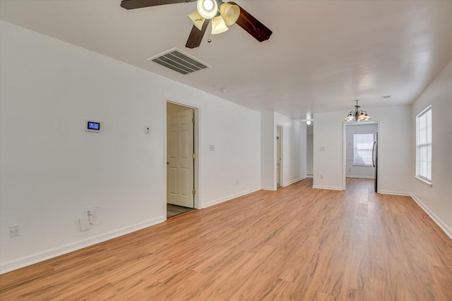 empty room with ceiling fan with notable chandelier and light hardwood / wood-style flooring