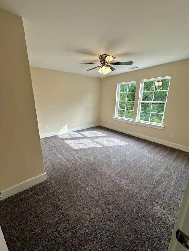 spare room with baseboards, dark carpet, visible vents, and ceiling fan