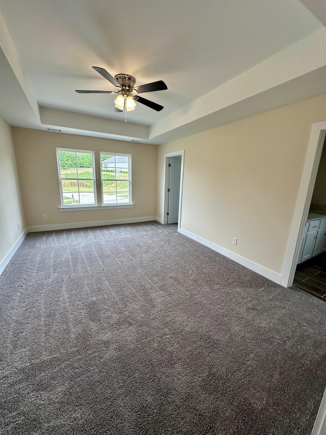 unfurnished room with a raised ceiling, a ceiling fan, and dark carpet
