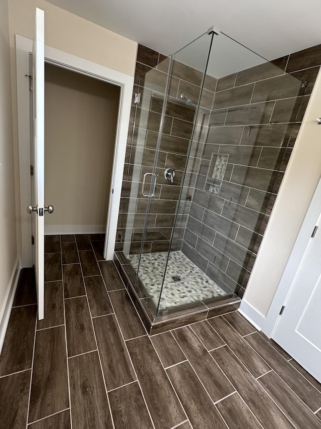 full bath featuring a stall shower, baseboards, and wood tiled floor