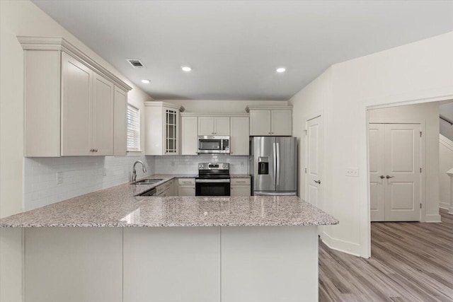 1404 Feldspar Ct, Augusta, GA 30909 - kitchen featuring stainless steel appliances, light wood-style flooring, a peninsula, light stone countertops, and decorative backsplash