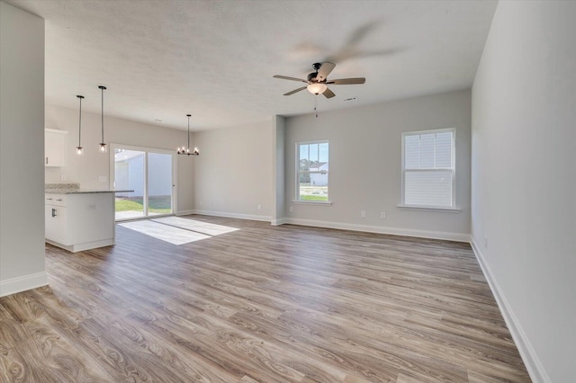 unfurnished living room with ceiling fan with notable chandelier, light wood-type flooring, and baseboards