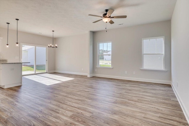 unfurnished living room with light wood-type flooring, visible vents, baseboards, and ceiling fan with notable chandelier