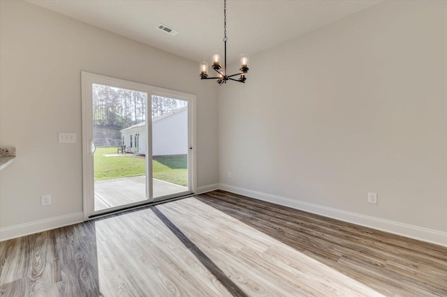 spare room with an inviting chandelier, visible vents, baseboards, and wood finished floors