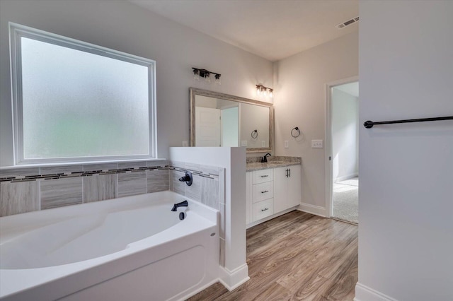 bathroom with baseboards, visible vents, wood finished floors, vanity, and a bath