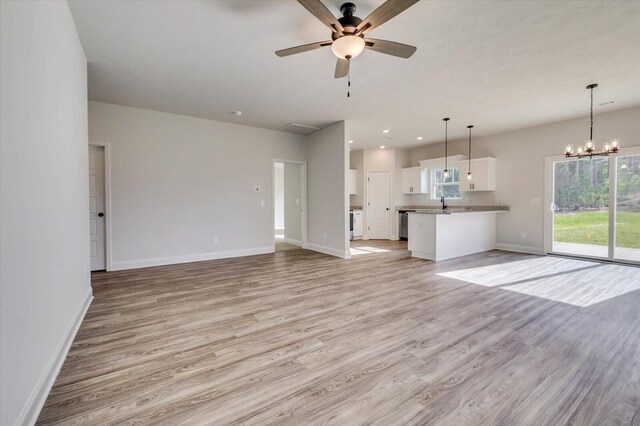 unfurnished living room with ceiling fan with notable chandelier, recessed lighting, light wood-style flooring, and baseboards