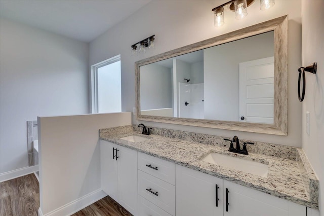 full bath with double vanity, a shower, a sink, and wood finished floors