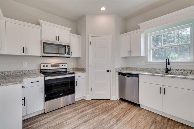 kitchen with light stone counters, stainless steel appliances, light wood-style floors, white cabinets, and a sink