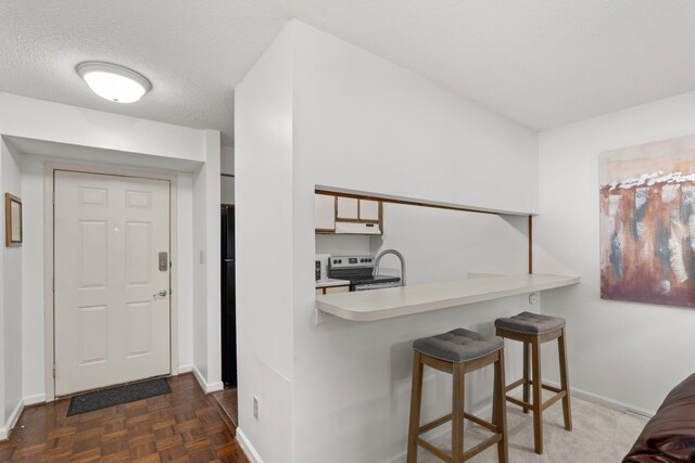 kitchen with dark parquet flooring, a kitchen breakfast bar, a textured ceiling, stainless steel electric stove, and white cabinetry