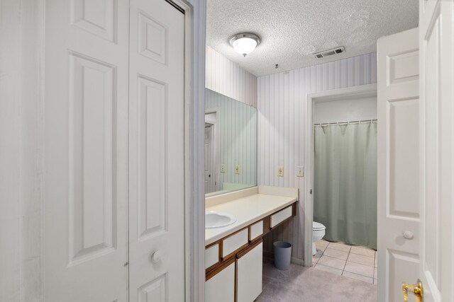 bathroom with tile patterned flooring, vanity, toilet, and a textured ceiling