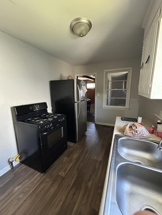 kitchen featuring dark wood finished floors, freestanding refrigerator, white cabinetry, black range with gas cooktop, and a sink