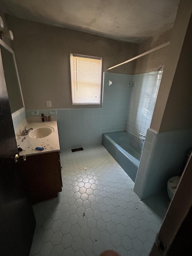 bathroom with toilet, a wainscoted wall, vanity, tile walls, and washtub / shower combination