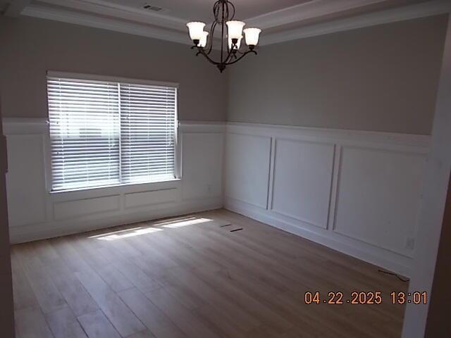 empty room featuring wainscoting, wood finished floors, an inviting chandelier, ornamental molding, and a decorative wall