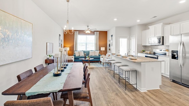 dining area featuring ceiling fan with notable chandelier, sink, and light hardwood / wood-style floors