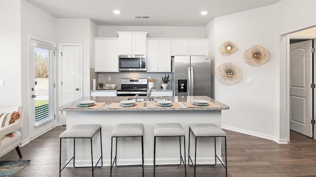 kitchen with white cabinetry, stainless steel appliances, a kitchen bar, and a kitchen island with sink