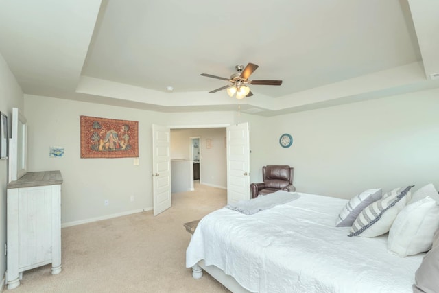 bedroom with a tray ceiling, light carpet, baseboards, and ceiling fan