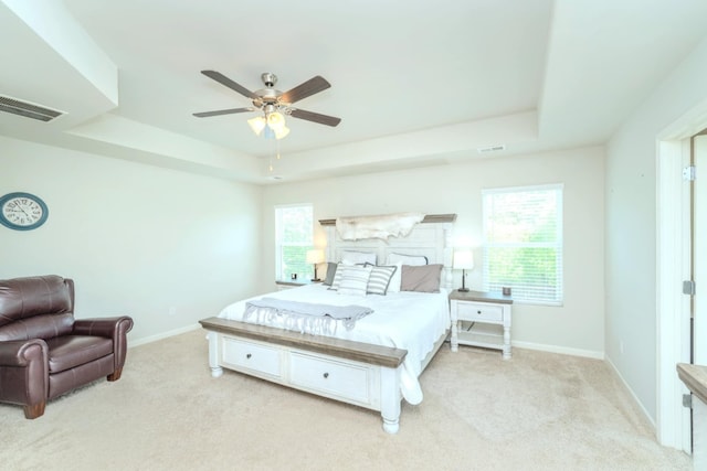 bedroom featuring a tray ceiling, light colored carpet, baseboards, and a ceiling fan