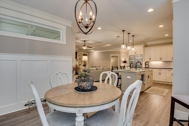 dining room featuring ceiling fan with notable chandelier, a raised ceiling, sink, crown molding, and light wood-type flooring