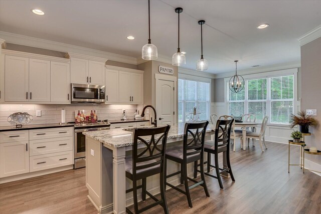 kitchen featuring appliances with stainless steel finishes, sink, pendant lighting, a center island with sink, and white cabinets