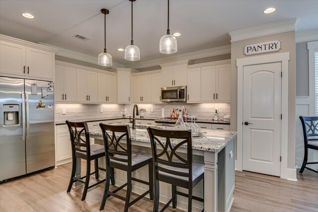 kitchen featuring white cabinets, appliances with stainless steel finishes, light stone counters, and a kitchen island with sink